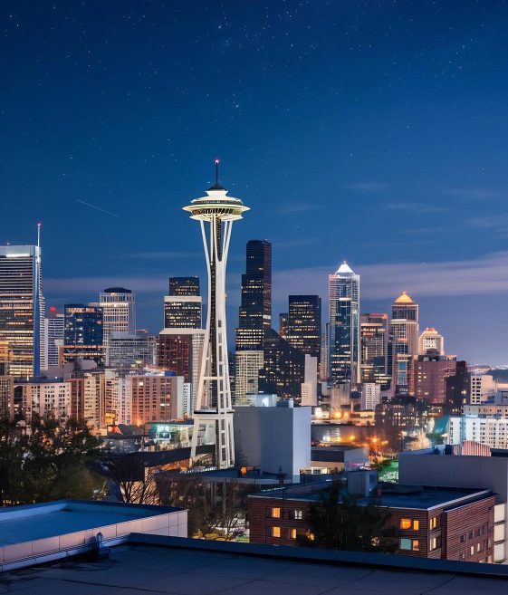 Seattle skyline at night with the Space Needle illuminated against a deep blue sky, surrounded by glowing downtown high-rises