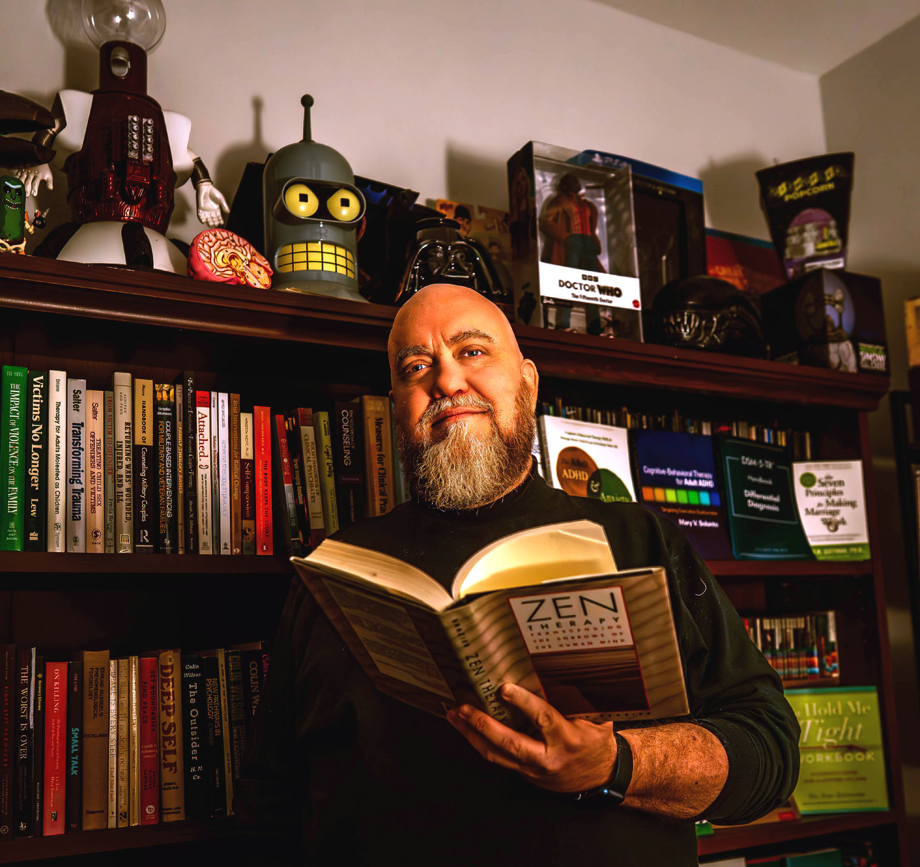 Jason standing in front of a bookshelf filled with psychology books and a bit of his nerdy collectibles