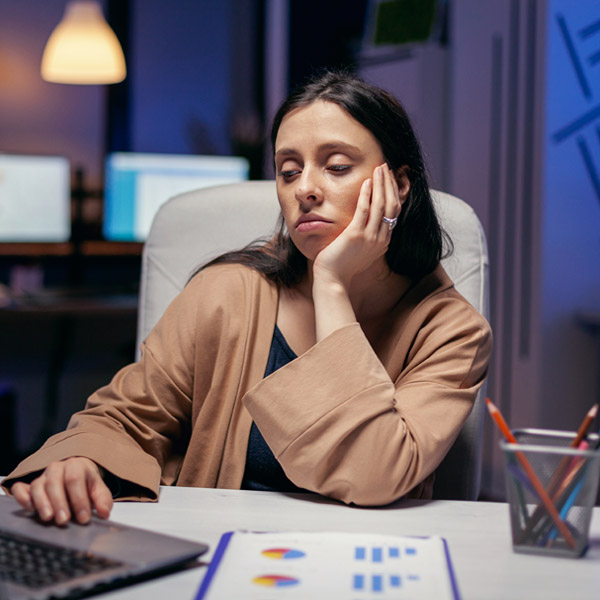 Exhausted businesswoman looking at computer working to finish a deadline. Smart woman sitting at her workplace in the course of late night hours doing her job.